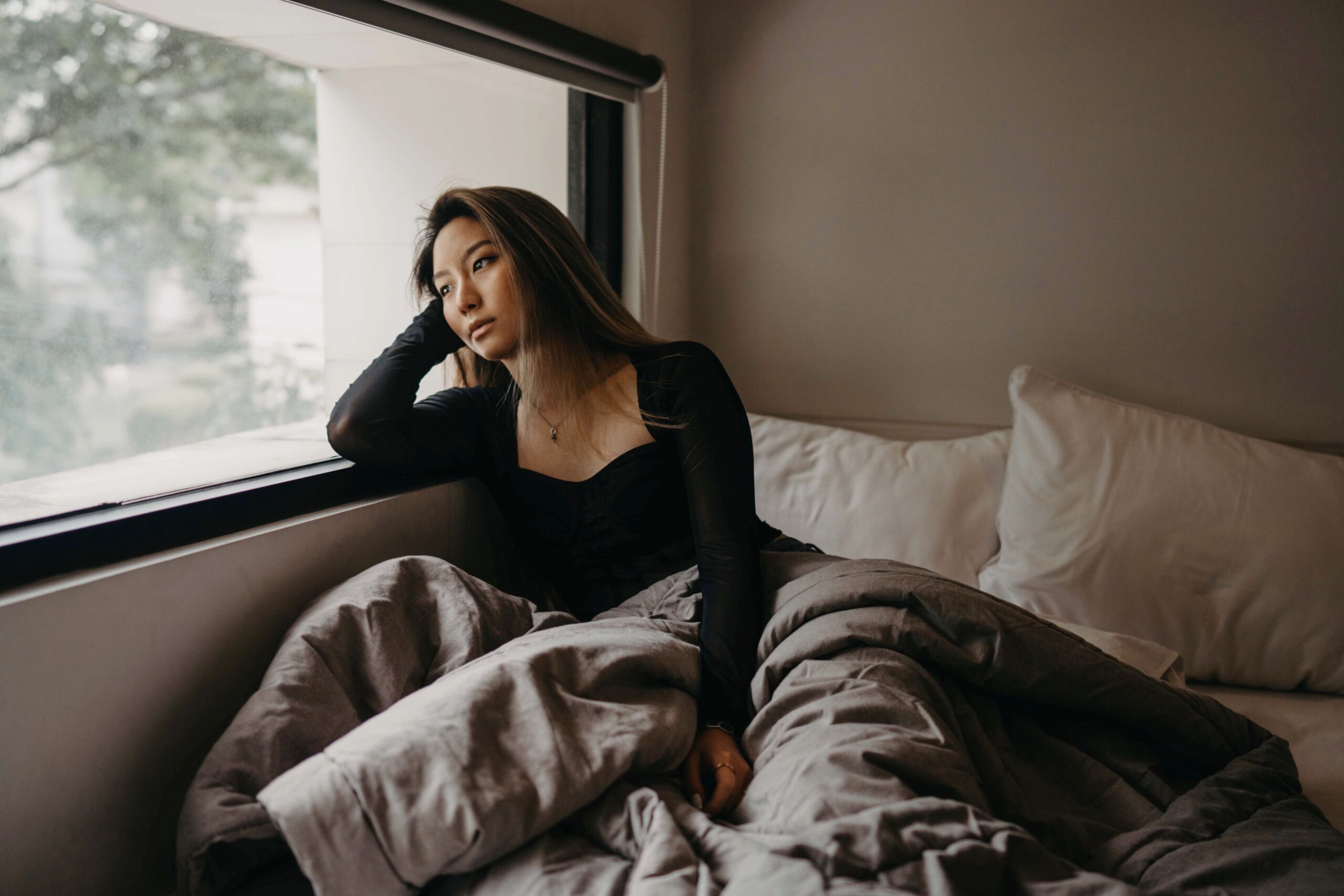 A woman sitting quietly near a window in soft morning light, reflecting on what it feels like to become disconnected from yourself.