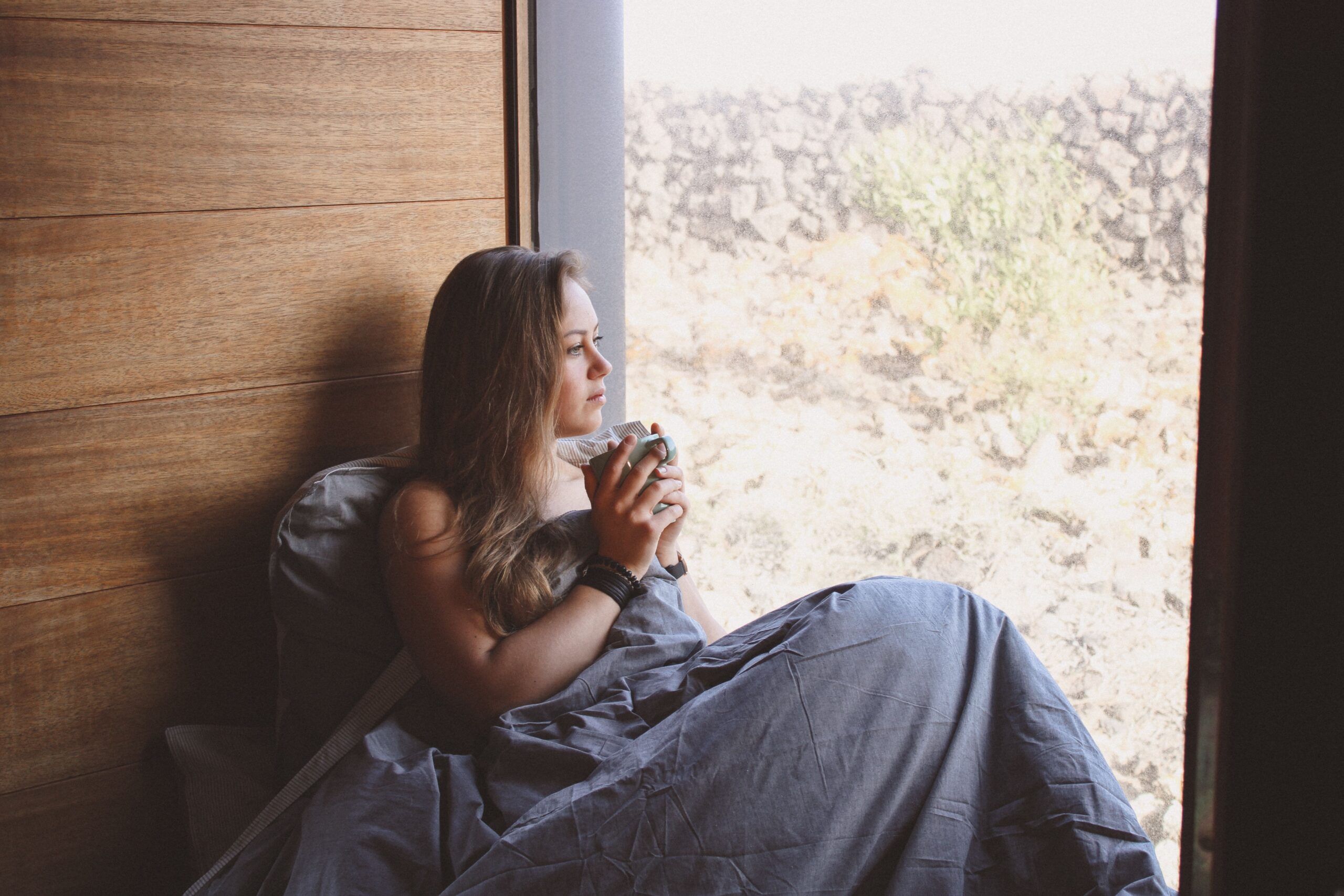 A woman sitting quietly near a window in soft morning light, reflecting on anxiety as a signal to return to herself.