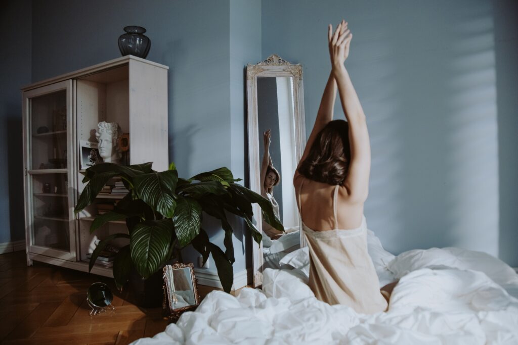 Woman stretching peacefully in bed in a quiet, sunlit bedroom